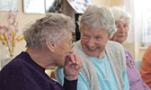 Foto: Seniorinnen sitzen am Tisch, essen Kuchen, lachen und unterhalten sich.